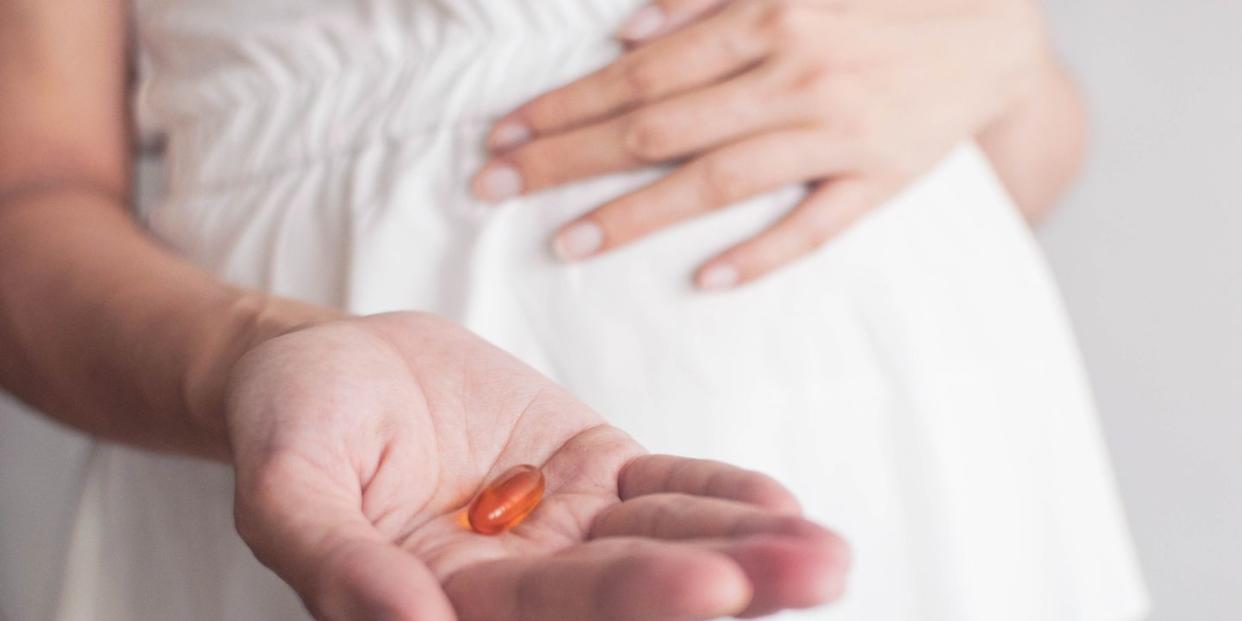a pregnant southeast asian woman is holding a medicine gel capsule