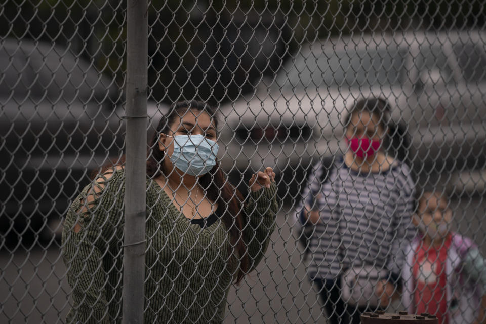 Griselda Saelak looks through a fence after dropping off her daughter on the first day of in-person learning at Heliotrope Avenue Elementary School in Maywood, Calif., Tuesday, April 13, 2021. More than a year after the pandemic forced all of California's schools to close classroom doors, some of the state's largest school districts are slowly beginning to reopen this week for in-person instruction. (AP Photo/Jae C. Hong)