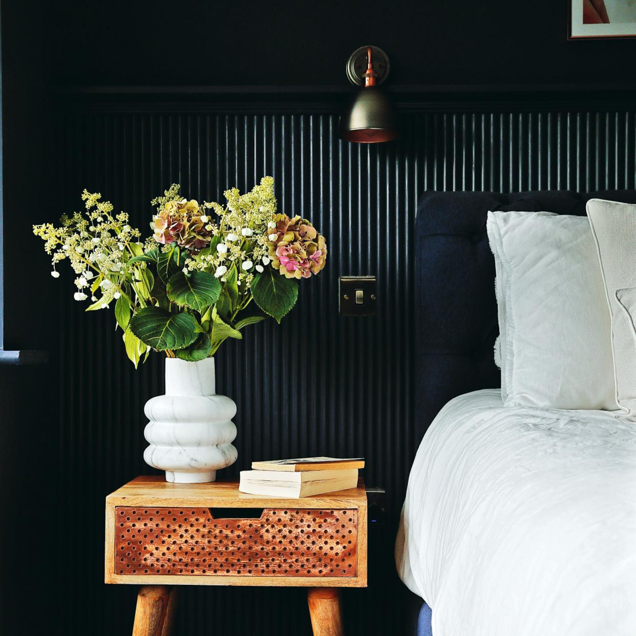  Flowers in white curved vase on wooden bedside table. 