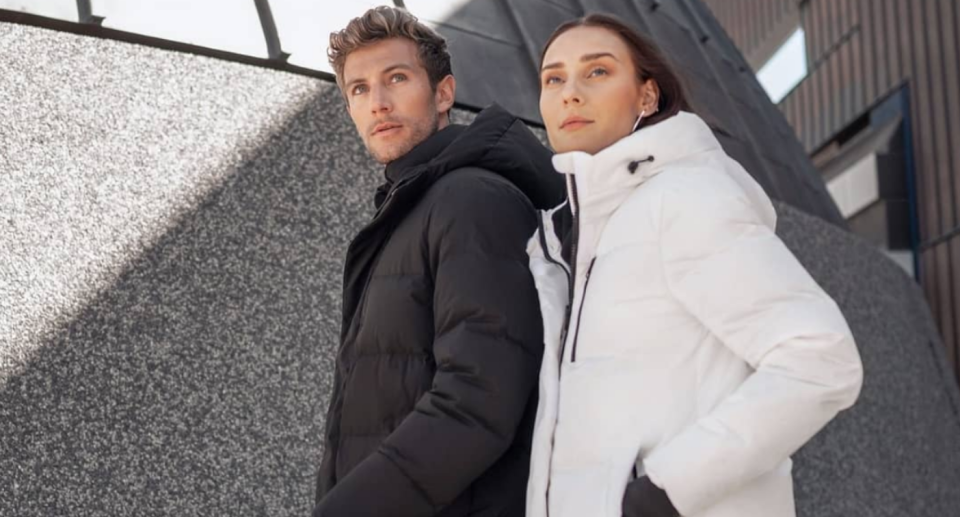 Man and woman pose while wearing winter jackets in an urban environment.