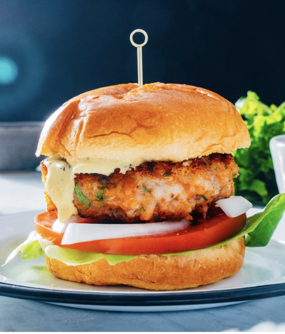 Burger with a crispy chicken patty, lettuce, tomato, and sauce on a brioche bun, skewered with a toothpick