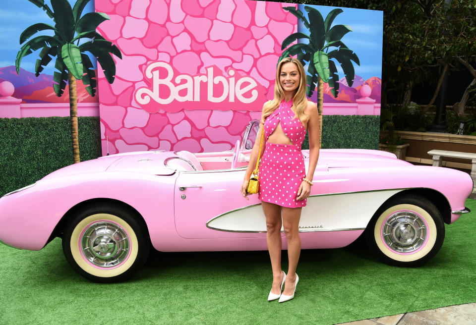 Margot Robbie poses in front of a Barbie car