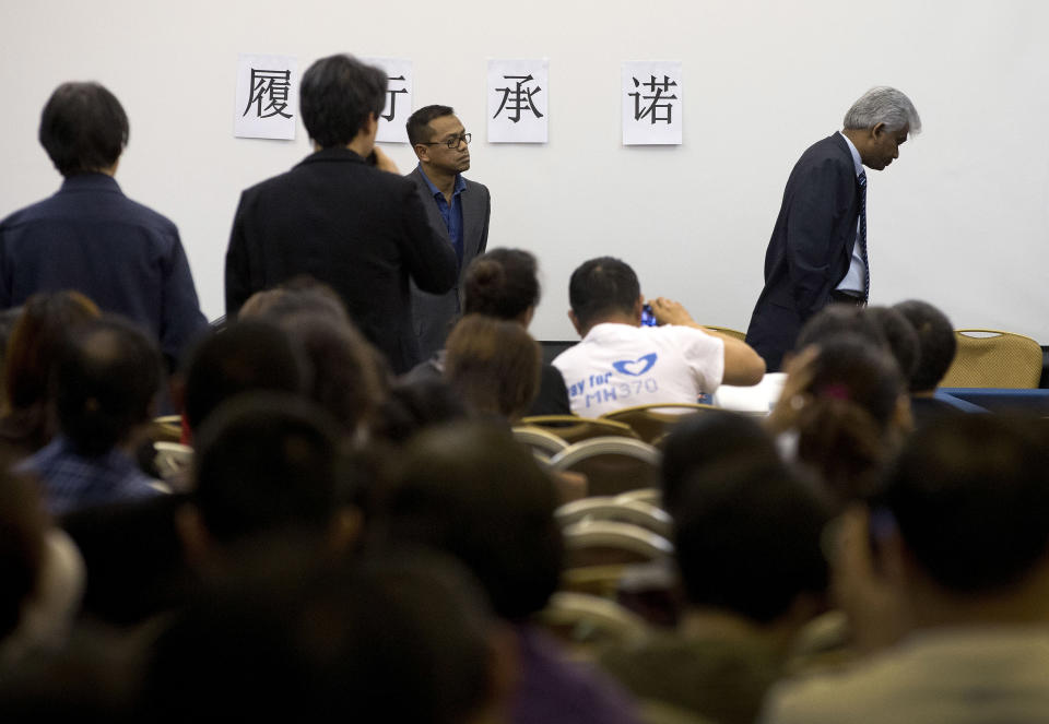 Bala Chandran Tharman, right, deputy chief of mission at the Malaysian embassy in Beijing walks away while relatives of Chinese passengers onboard the Malaysia Airlines MH370 ask him a question during a briefing at a hotel in Beijing, China, Saturday, April 26, 2014. A number of Chinese relatives still aren't accepting the theory that the plane crashed in the Indian Ocean. They're insisting that Malaysian officials haven't told them the truth. The Chinese characters on the wall reads: "Meet the commitment." (AP Photo/Andy Wong)