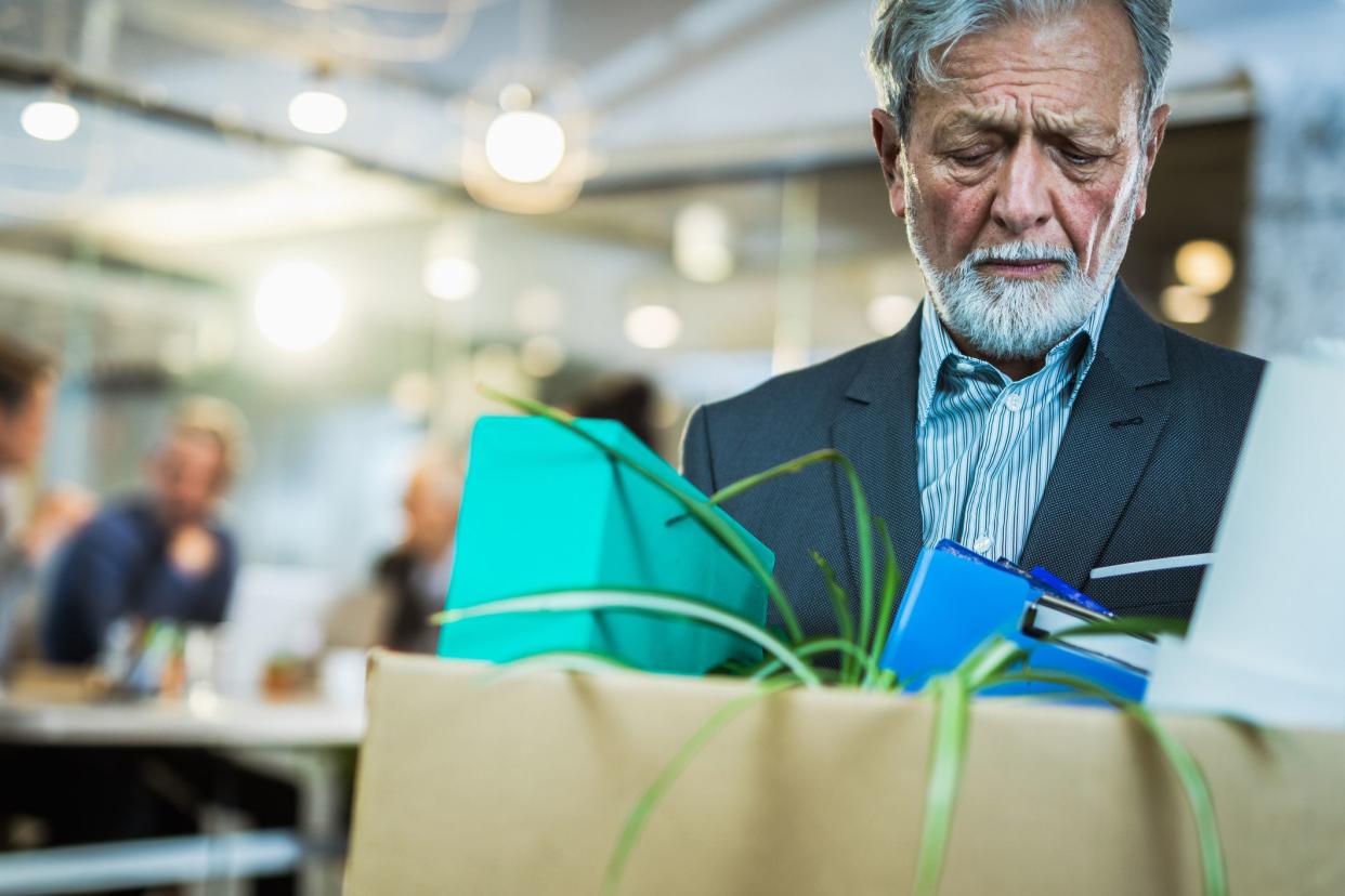 sad senior employee leaving office with cardboard box of stuff