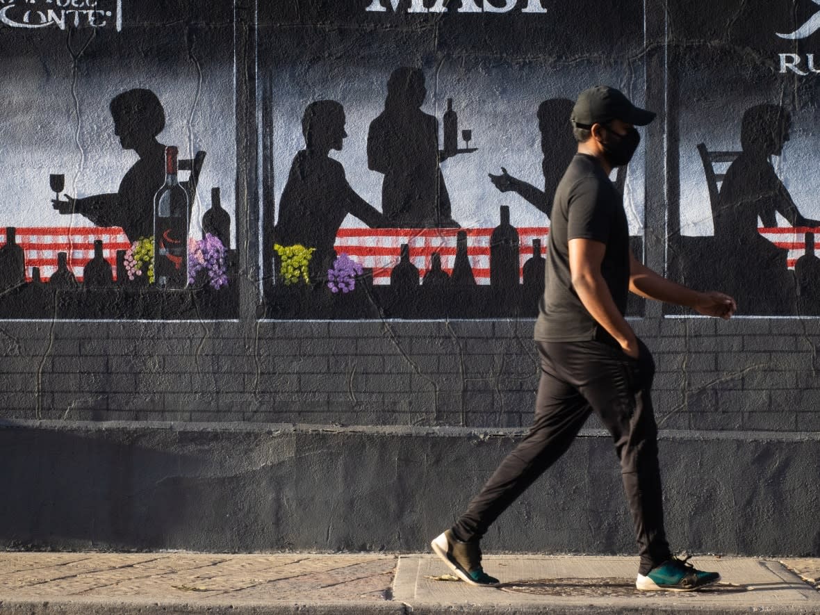 A pedestrian in a mask walks past a mural adorning the side of a restaurant in Ottawa's Little Italy neighbourhood on Oct. 22, 2021. (Trevor Pritchard/CBC - image credit)