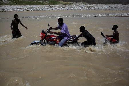 Boys help a man to cross a river as he drives a motorbike after Hurricane Matthew in Les Anglais, Haiti, October 10, 2016. REUTERS/Andres Martinez Casares