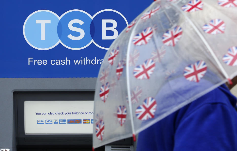 A pedestrian shelters from the rain beneath a British Union flag themed umbrella as they pass an automated teller machine (ATM) outside a TSB bank branch. Photo: Chris Ratcliffe/Bloomberg via Getty Images