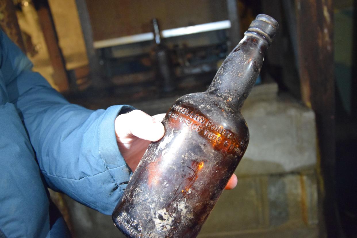 Taylor Dueweke holds a bottle found in the basement of the former Club Manitou site. The bottle is a Haig & Haig bottle and includes a disclaimer saying federal law prohibits the reuse of the bottle.