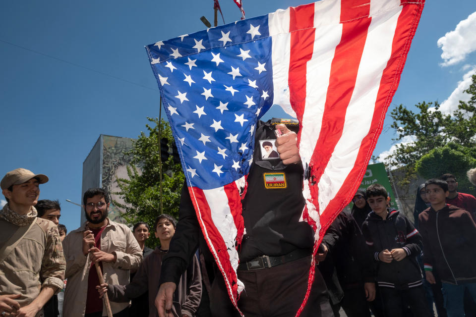 An Iranian protester with a portrait of Iran's Supreme Leader Ayatollah Ali Khamenei on his fake military uniform burns the US flag during a rally commemorating the International Quds Day in downtown Tehran, on April 14, 2023.