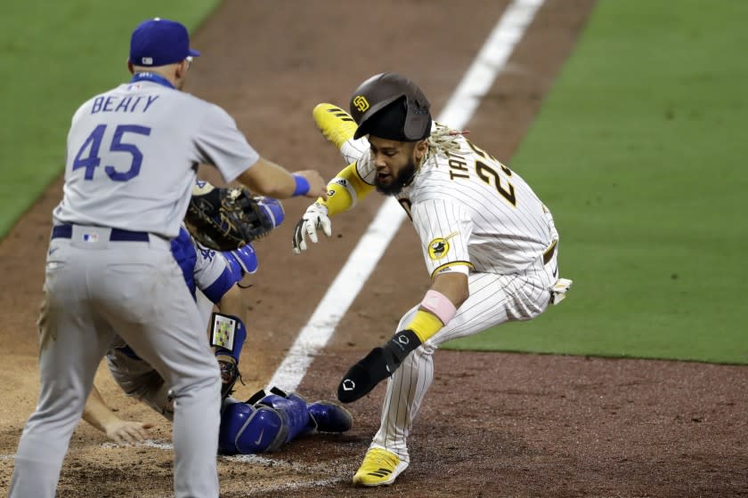 San Diego Padres' Fernando Tatis Jr., right, is tagged out by Los Angeles Dodgers catcher Will Smith, behind center, attempting to score from third off a line out by Manny Machado as Los Angeles Dodgers first baseman Matt Beaty (45) looks on, left, during the seventh inning of a baseball game Monday, Aug. 3, 2020, in San Diego. (AP Photo/Gregory Bull)