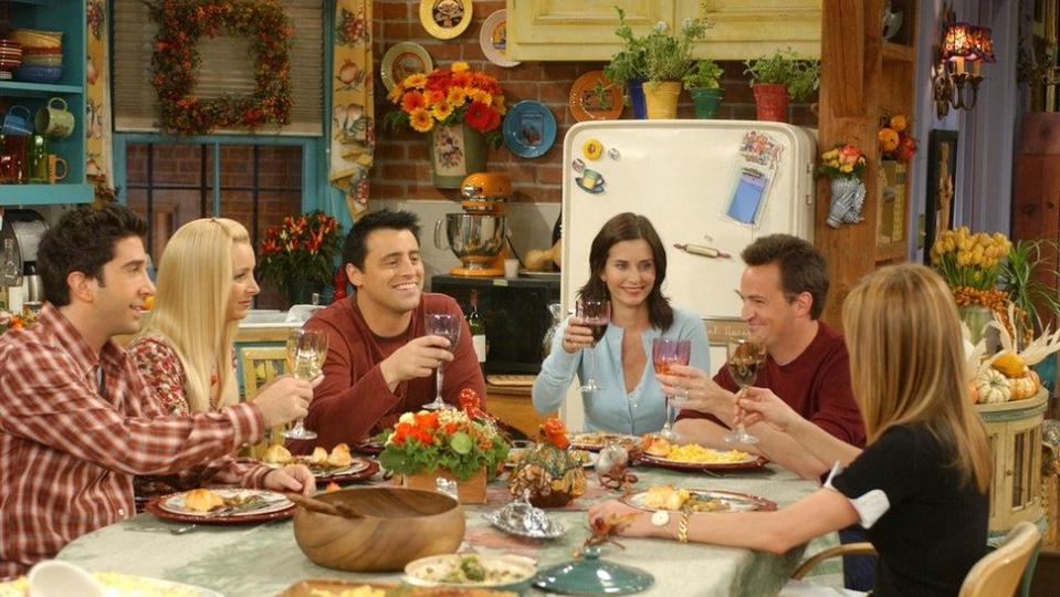 ross, phoebe, joey, monica, chandler and rachel from tv show friends gathered around table raising glasses in a toast