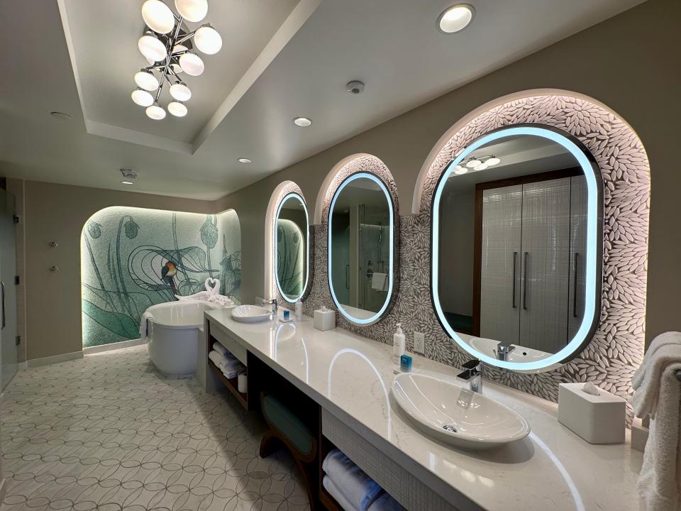 Bathroom with long counter, deep bathtub, Bambi mural, and three large mirrors with lights around it in Disney villa.