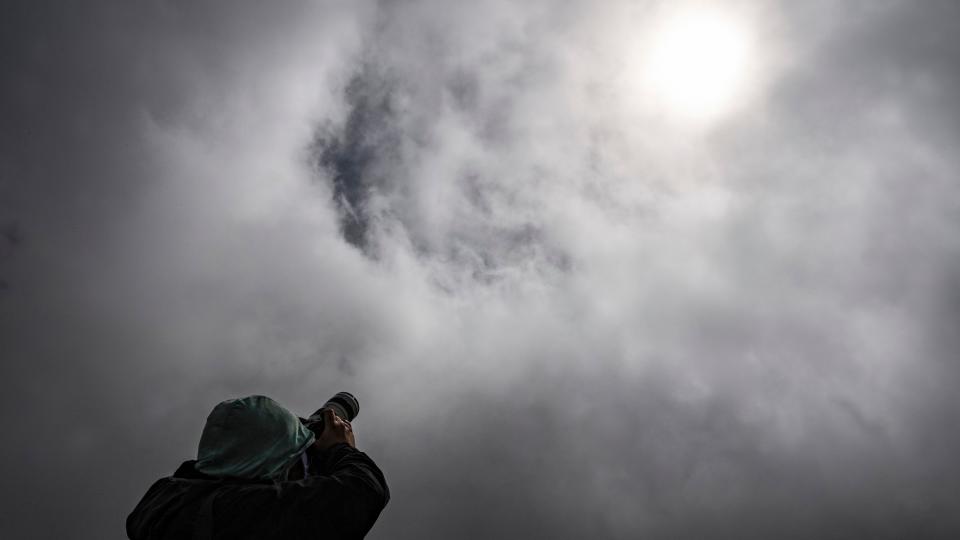 a person looks up at a cloudy sky with the sun shining through the clouds.