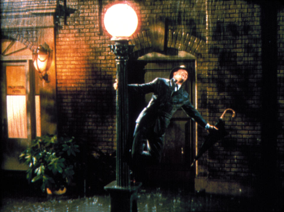 Gene Kelly swings happily in the rain on a lamppost while holding an umbrella in a scene from "Singing in the rain."