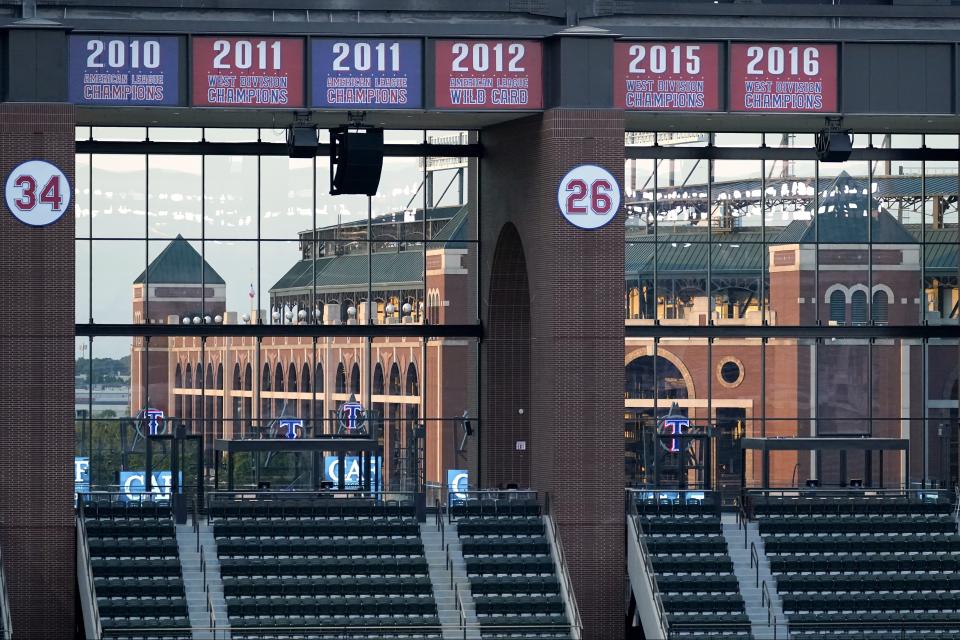 Championship pennants and retired numbers over the left field seating at Globe Life Field are displayed in the foreground as the teams former park, Globe Life Park is seen through the windows as the Texas Rangers play against the Houston Astros in the fourth inning of a baseball game in Arlington, Texas, Saturday, Sept. 26, 2020. (AP Photo/Tony Gutierrez)