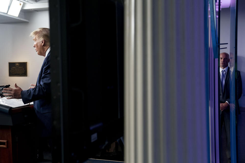 A member of the Secret Service stands guard, right, as President Donald Trump, left, speaks at a news conference in the James Brady Press Briefing Room at the White House, Monday, Aug. 10, 2020, in Washington. Trump briefly left because of a security incident outside the fence of the White House. (AP Photo/Andrew Harnik)