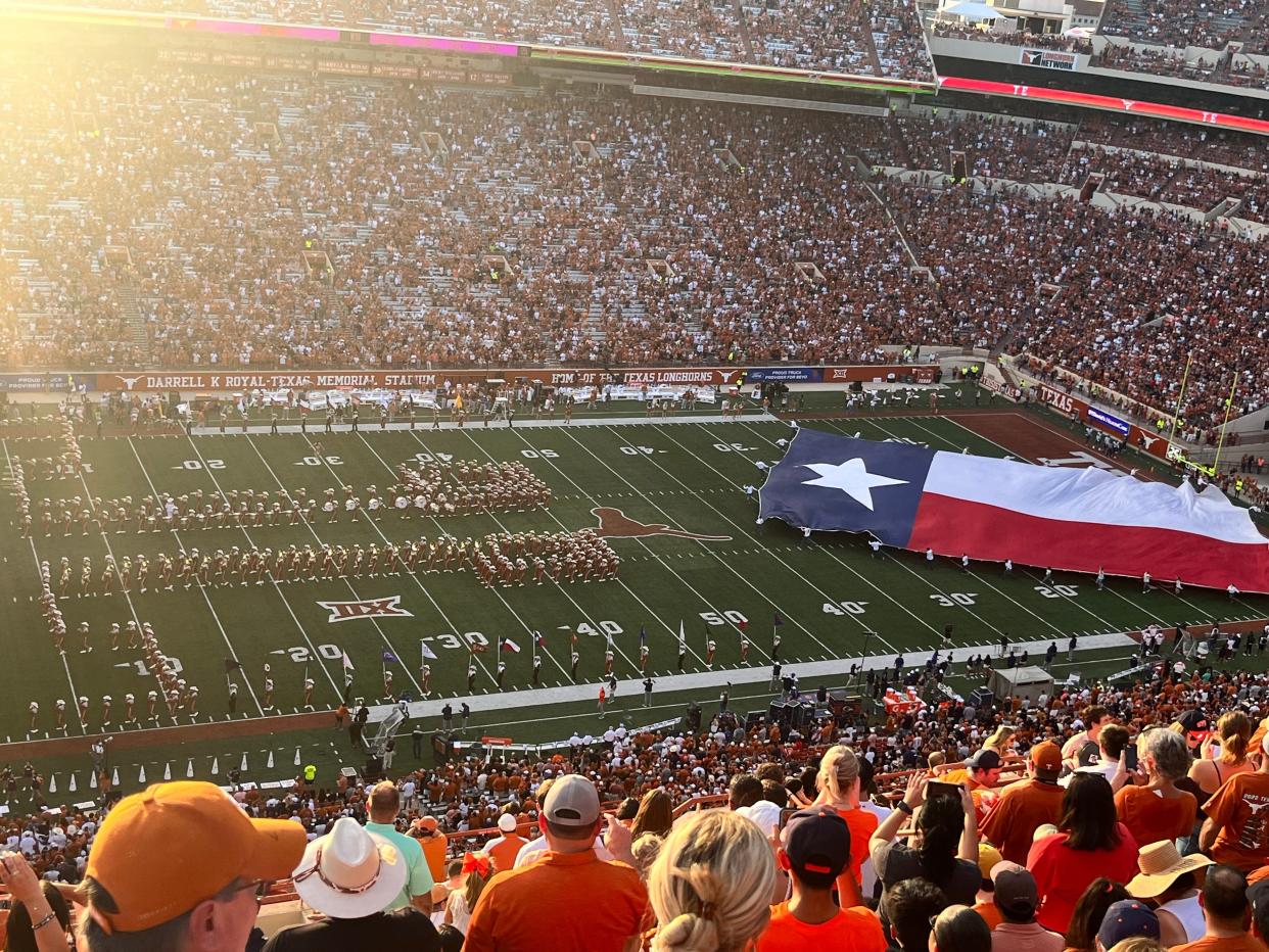 Crowds of people dressed in orange at a University of Texas football game as a Texan flag is dragged onto the field.