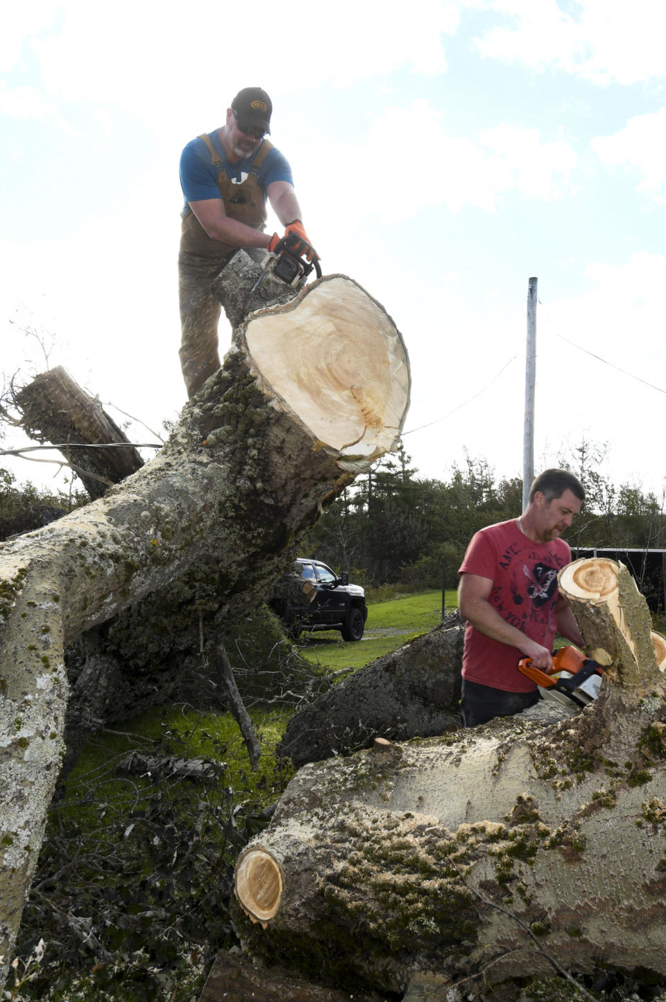 Workers Darren MacKinnon, left, and Derek Facchin cut into a fallen tree in Reserve, Nova Scotia, on Sunday, Sept. 25, 2022. Hundreds of thousands of people in Atlantic Canada remain without power and officials are trying to assess the scope of devastation from former Hurricane Fiona. It swept away houses, stripped off roofs and blocked roads across the country’s Atlantic provinces. (Vaughan Merchant/The Canadian Press via AP)