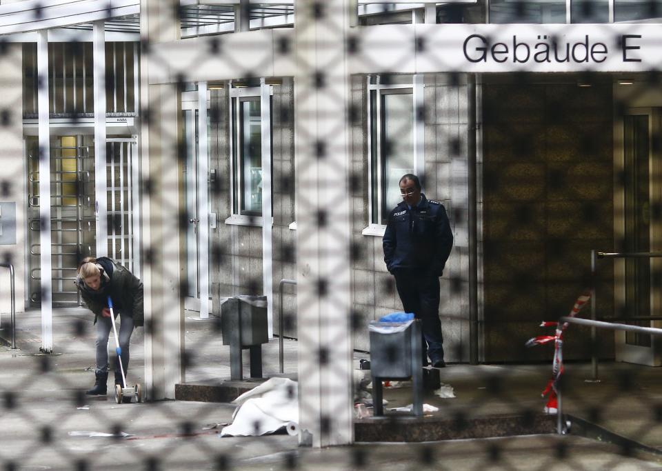 Police officer examines crime scene next to covered body at entrance to courthouse in Frankfurt