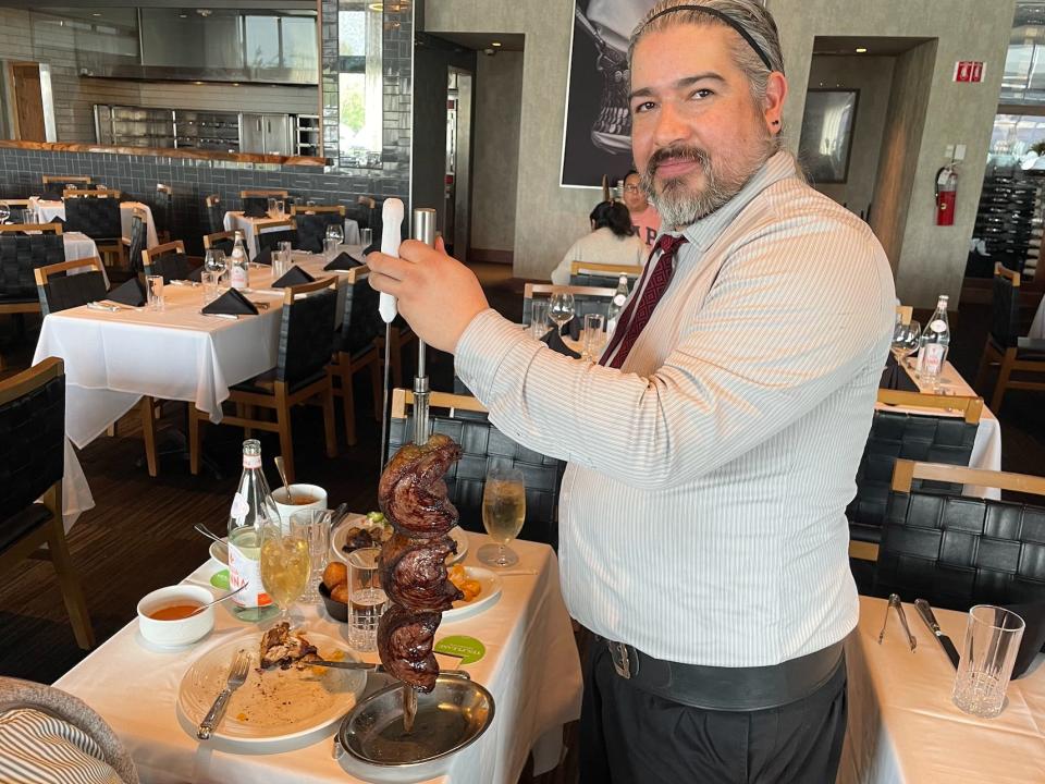 a server presenting a skewer of meat at fogo de chao steak house