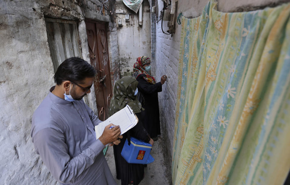 A health worker collects data while another writes numbers on the wall of a house after administrating a polio vaccine to children in a neighborhood of Lahore, Pakistan, Monday, Aug. 2, 2021. The government launched polio vaccination drives across Pakistan in efforts to eradicate the crippling disease by the end of the year. (AP Photo/K.M. Chaudhry)