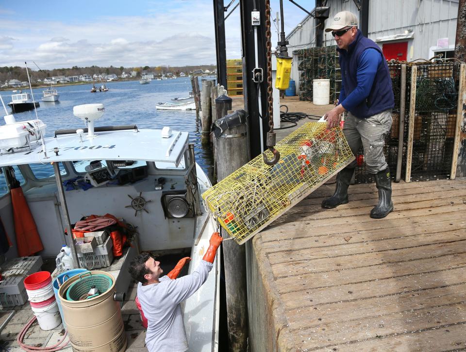Lobstermen Riley Austin, left, and Ed Hutchins load the Christina Mae II with traps on the Cape Porpoise pier in May 2022. Next week, the state will celebrate them and others in their industry during Maine Lobster Week.