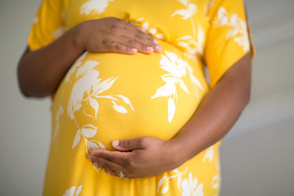 Young pregnant woman holding her stomach smiling.