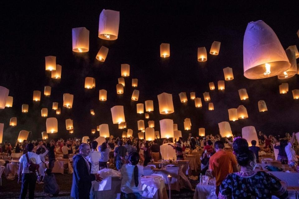 People release glowing sky lanterns into the night at a crowded outdoor festival