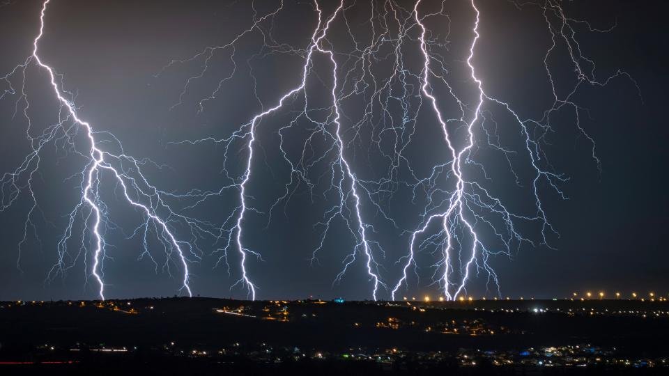 multiple lightning strikes on a black sky with a town below