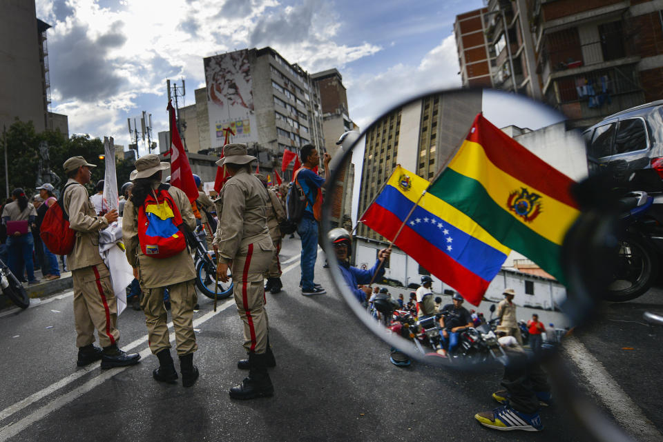 Reflected in a motorcycle side mirror, supporters of Venezuelan President Nicolas Maduro rally in support of former Bolivian President Evo Morales in Caracas, Venezuela, Monday, Nov. 11, 2019. Morales stepped down following weeks of massive protests. (AP Photo/Matias Delacroix)