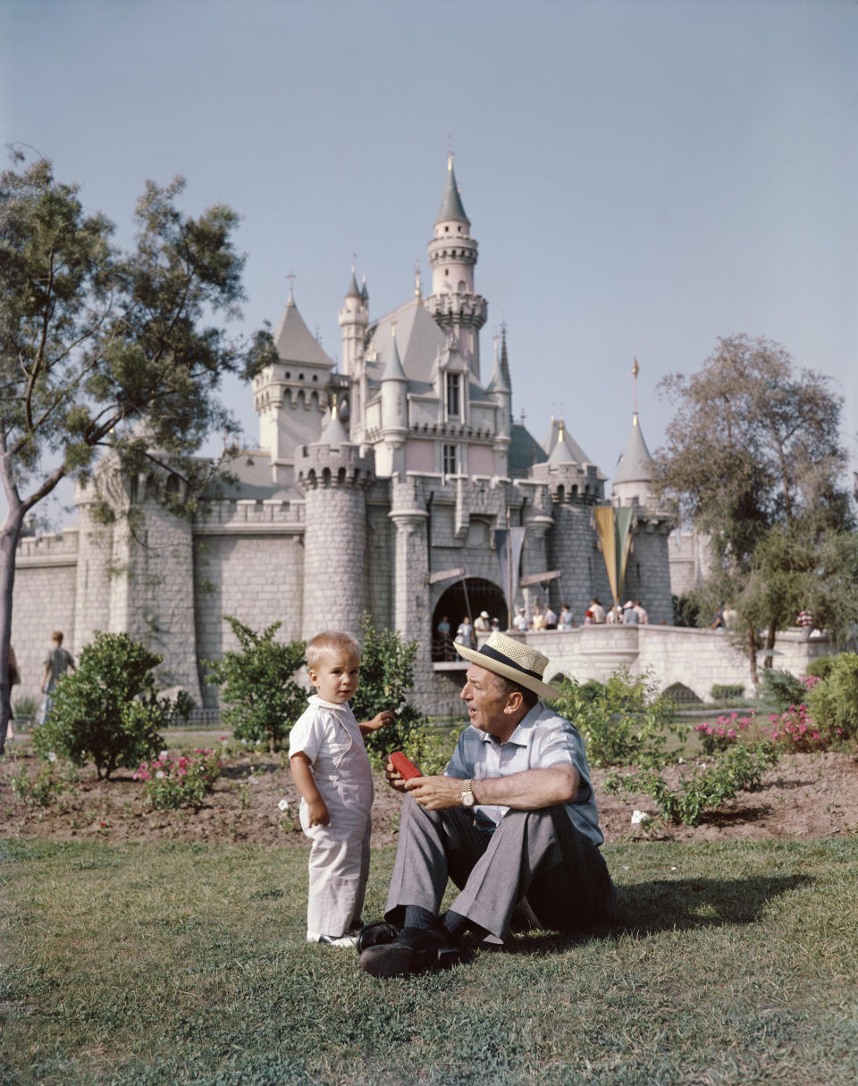 Walt Disney sitting with a young boy in front of Disneyland's Sleeping Beauty Castle