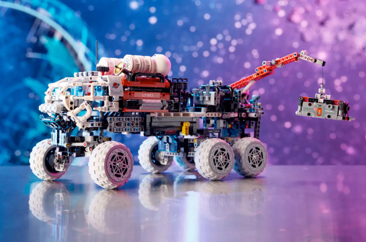  Photo of a multicolored LEGO rover on a shiny table against a purple and blue cosmic-themed backdrop. 