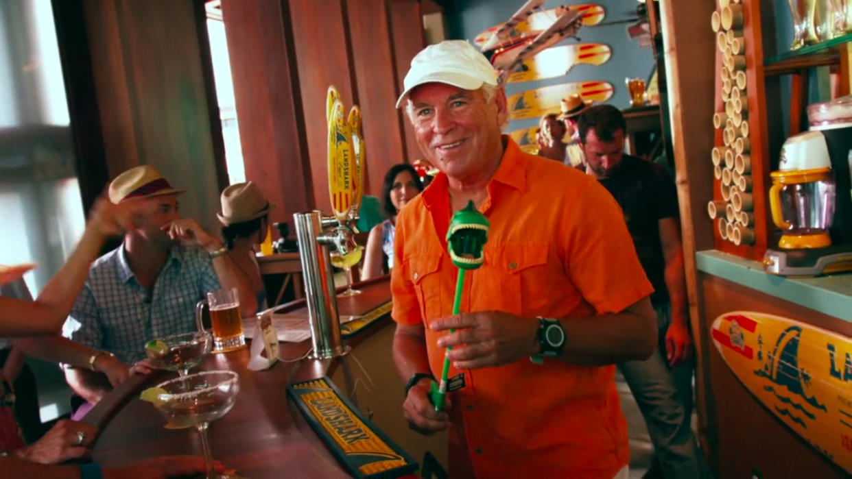  Jimmy Buffett standing behind the bar with a dinosaur toy in hand on the set of Jurassic World. 