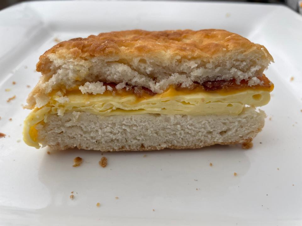 Breakfast sandwich with biscuit, egg, cheese, and bacon cut in half on a plate