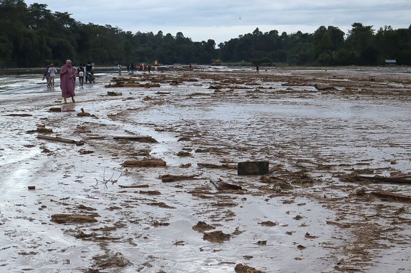 People pass through mud on a runway at Andi Jemma Masamba airport, after flash floods killed several people and dozens remain missing, in North Luwu, Indonesia