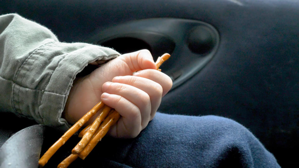 Child's hand clutching pretzel sticks while sitting in a car seat