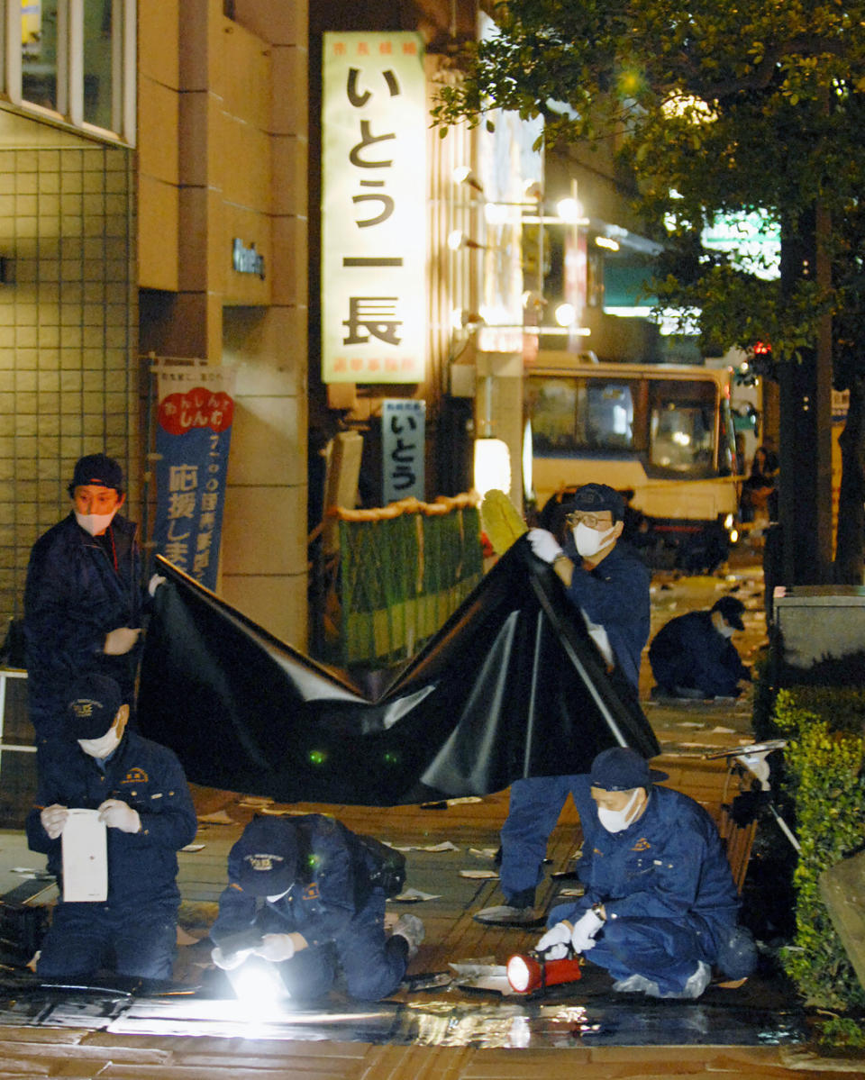 FILE - Police officers investigate at the site where Nagasaki Mayor Iccho Ito was assassinated by gunshot, in Nagasaki, southern Japan, April 17, 2007. Gang violence in a number of neighborhoods, including the 2007 fatal shooting of Ito during his election campaign, have since led the government to tighten gun control, racketeering laws and other anti-gang measures. (Kyodo News via AP, File)