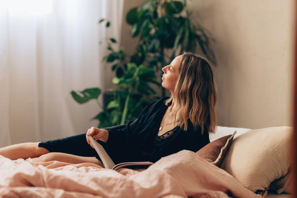 A happy young woman sitting on the bed in a black nightgown, reading the newspaper.