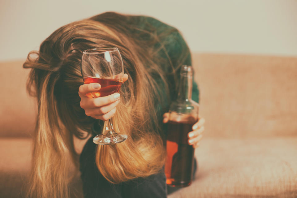 Depressed woman drinking  alcohol while sitting alone at sofa.Toned image.