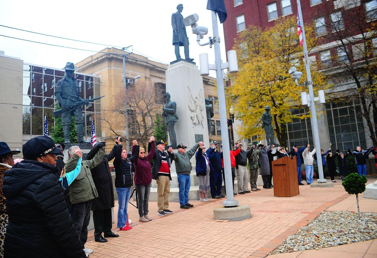 Attendees raise their hands in unison as Lee Greenwood's "God Bless the U.S.A." plays during the Veterans Day service at Freedom Square in downtown Alliance on Saturday, Nov. 11, 2023.