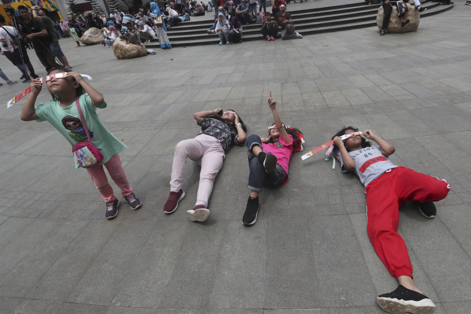 People look up at the sun wearing protective glasses to watch a solar eclipse in Jakarta, Indonesia, Thursday, Dec. 26, 2019. (AP Photo/Tatan Syuflana)