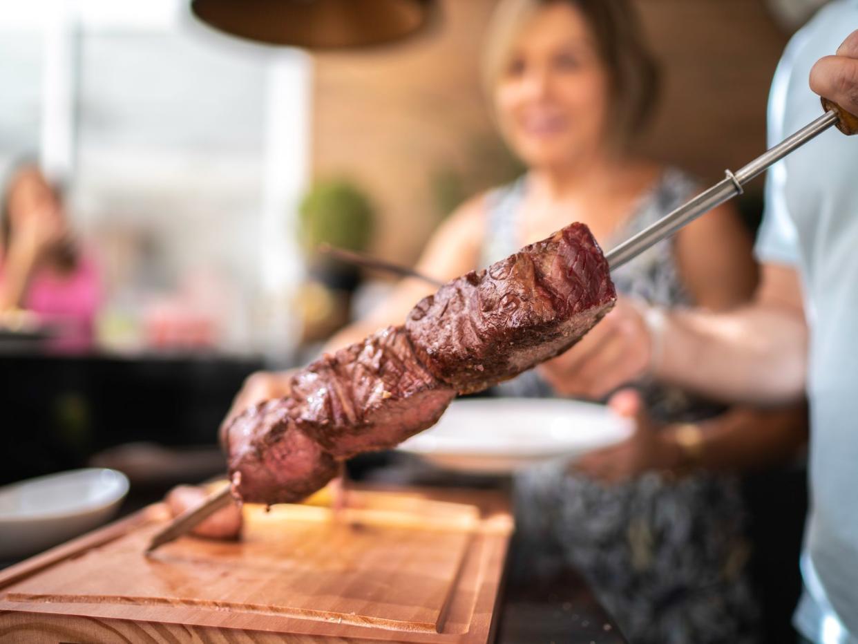 Focus on man's hand cutting picanha meat during barbecue