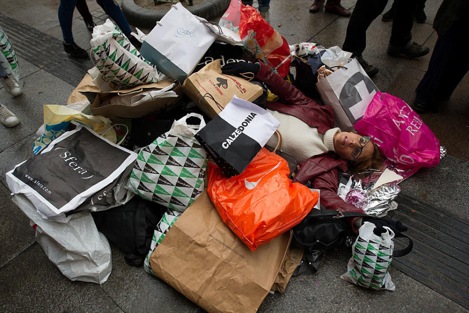 A woman laying on the street with many shopping bags sprawled over her.