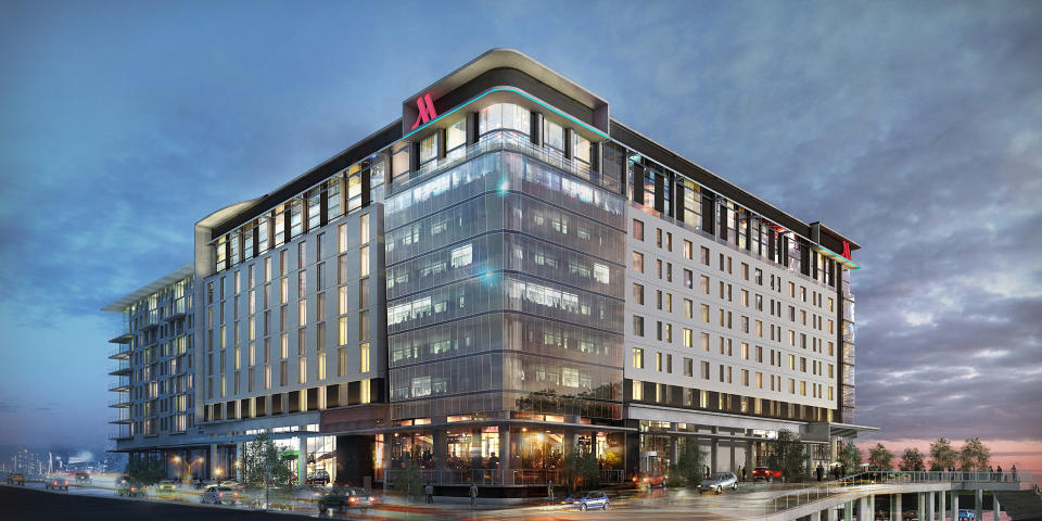 Multistory hotel with Marriott logo against a cloudy sky with near-empty road in front.