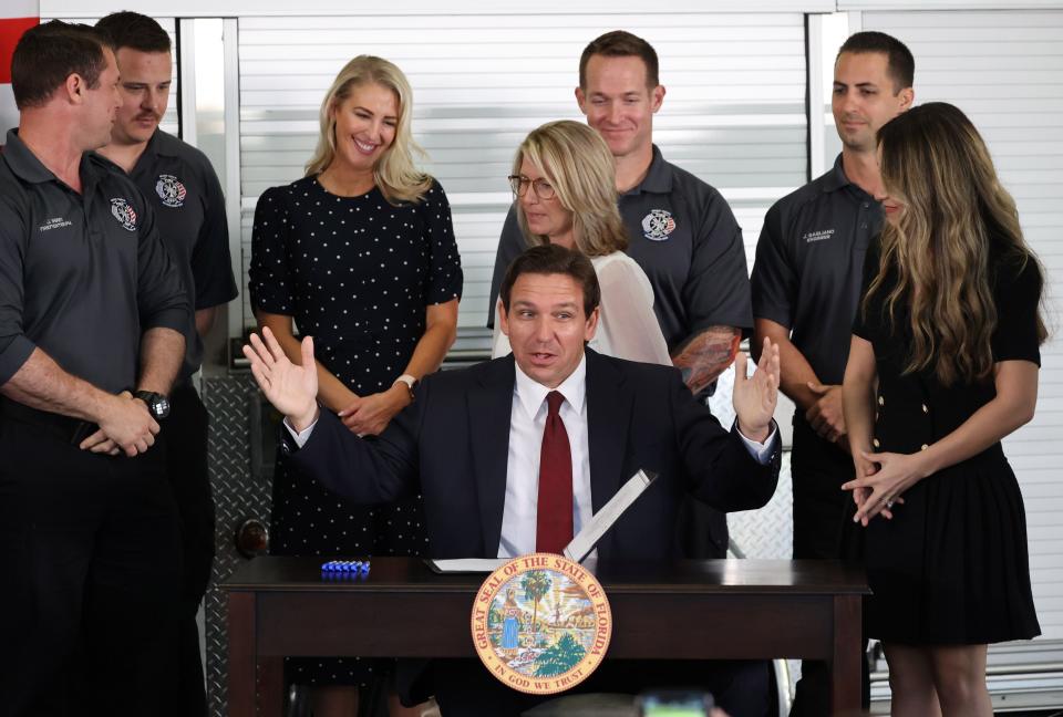Florida Governor Ron DeSantis sits at a desk to sign a bill.