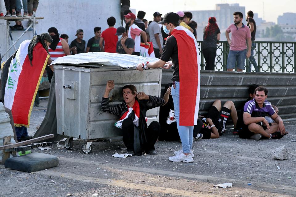 Anti-government protesters take cover while security forces use tear gas to disperse them, on the closed Sinak Bridge that leads to the Green Zone government areas in Baghdad, Iraq, Sunday, Oct. 25, 2020. Thousands of Iraqi protesters have taken to the streets to mark one year since mass anti-government demonstrations swept Baghdad and Iraq's south. Protesters marched Sunday in the capital and several southern cities to renew demands to bring an end to corruption perpetuated by Iraq's politicians. (AP Photo/Khalid Mohammed)