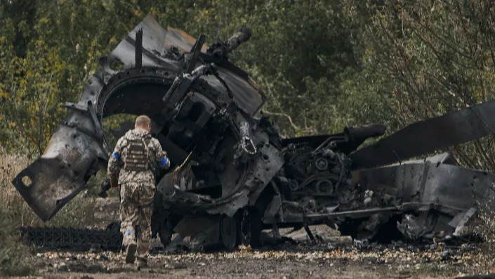 A Ukrainian soldier passes by a Russian tank 