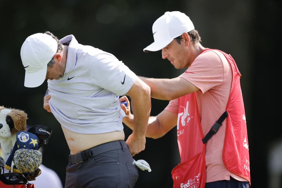 Rory McIlroy, left, has pain-relieving balm applied to his back by his caddie Harry Diamond, right, during the first round of the Tour Championship golf tournament at East Lake Golf Club, Thursday, Aug. 24, 2023, in Atlanta. (AP Photo/Alex Slitz)