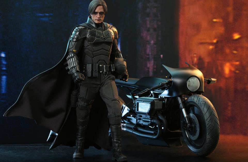 Hot Toys' The Batman figure without his mask on standing in front of his Batcycle