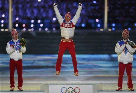 Russia's gold medallist Alexander Legkov jumps on the podium between compatriots silver medallist Maxim Vylegzhanin (L) and bronze medallist Ilia Chernousov (R) as they are presented with medals for the men's cross-country 50km mass start free event during the closing ceremony of the 2014 Sochi Winter Olympics, February 23, 2014. REUTERS/Phil Noble